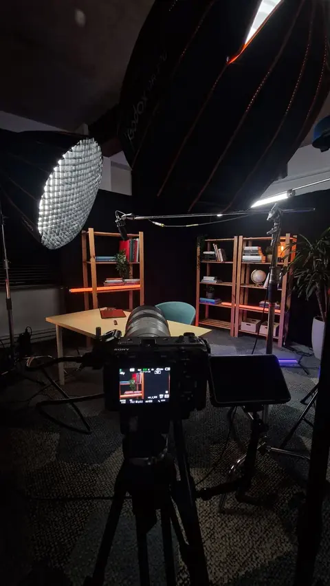 A camera and lighting equipment in front of a seated recording setup.